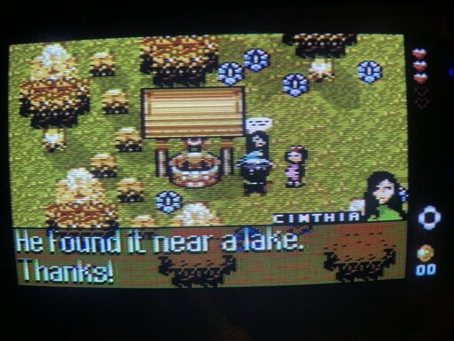 Screenshot of Lykia for the Commodore 16 showing a beautiful scene near a well with three people talking. The style is a 2D JRPG