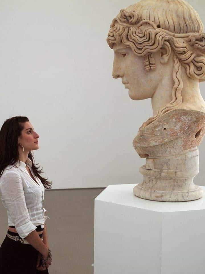 A Greek woman examines an antique statue (circa 130 AD, from the Villa Mondragone of the Borghese princes in Frascati). Louvre, Paris. year 2013.