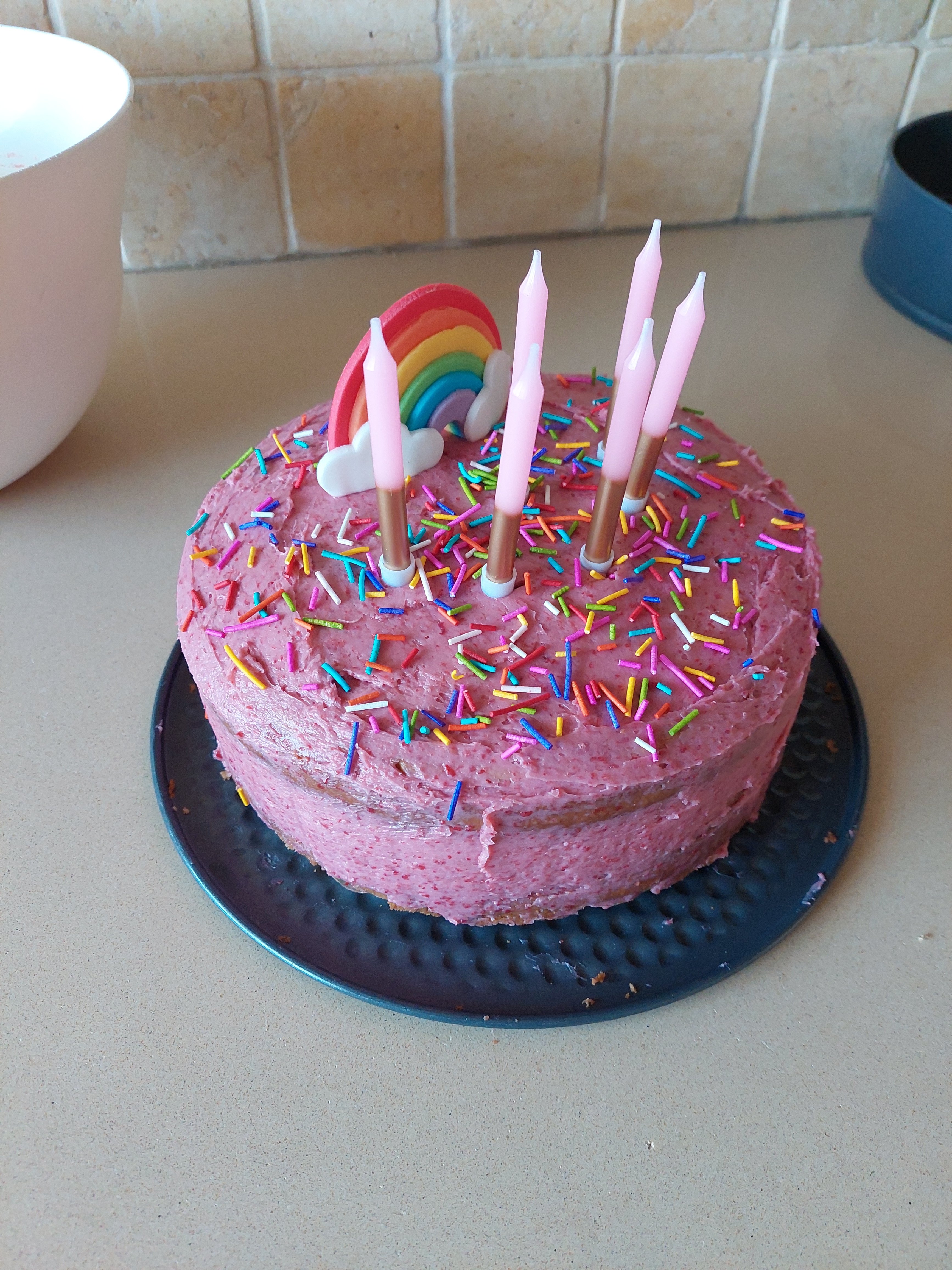 a picture of the full cake with 6 candles and a fondant rainbow decoration