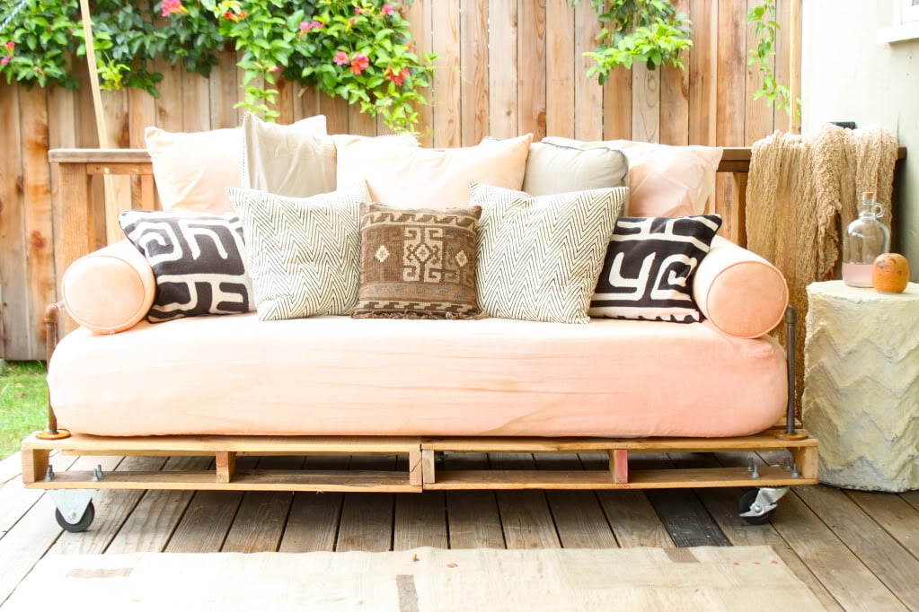 A daybed on a patio, made from pallets and industrial pipe